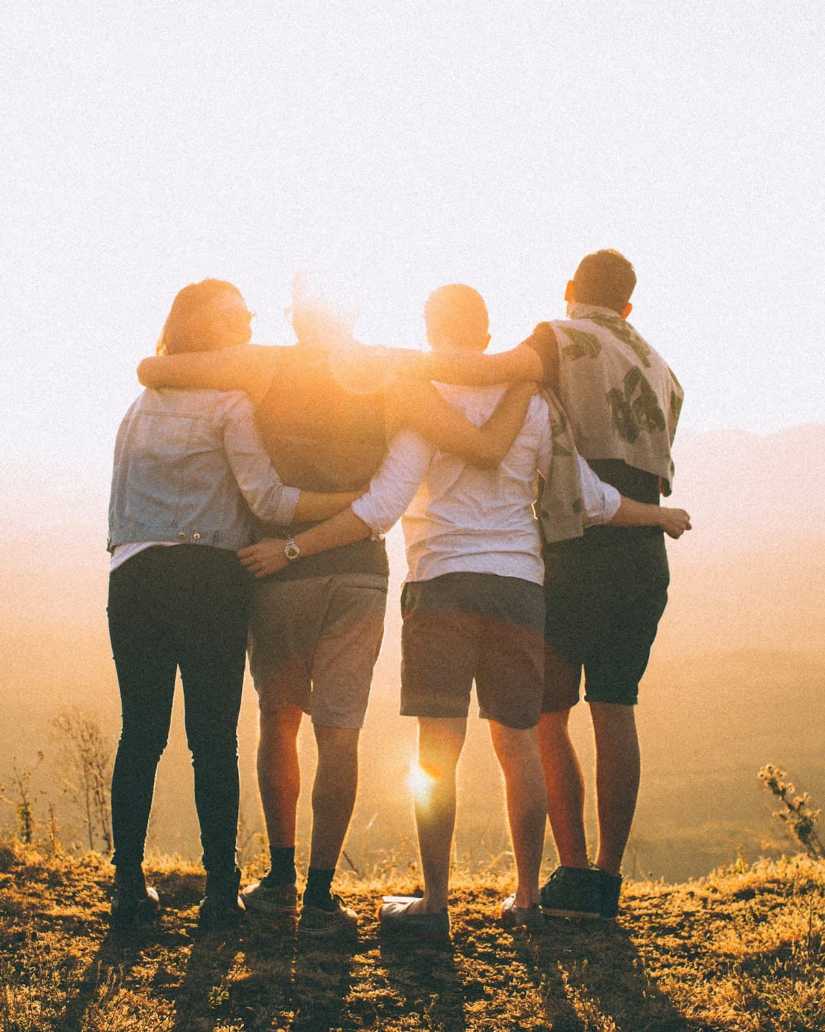 Four friends with arms around each other, looking out at the sunset.